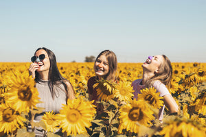 Three women in a sunflower field with colorful sunscreen on noses